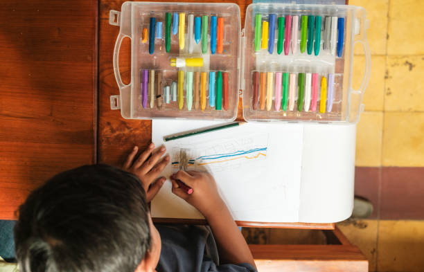 a top view of an asian boy while he is drawing using his crayons and pencils on the table, Science, Technology, Education, Mathematics or STEM concept stock photo