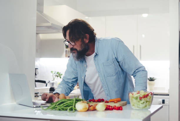 istock One man at home preparing fresh healthy salad using online tutorial. Modern people cooking vegetables looking for help on laptop and internet connection. Modern adult using computer to find recipes 1458997191