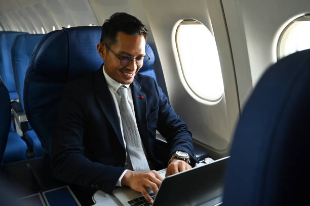 istock Successful millennial businessman in black suit using laptop while sitting in airplane cabin. 1458998773