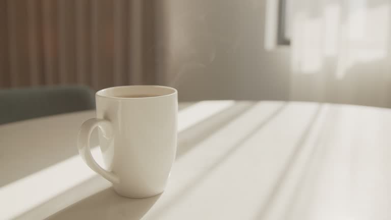 Mug of hot coffee steaming on the kitchen table with warm morning sunlight coming through the window