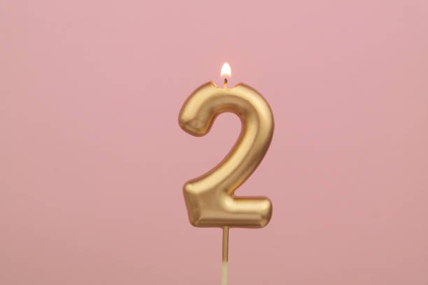 Gold birthday candle on pink background, number 2 stock photo