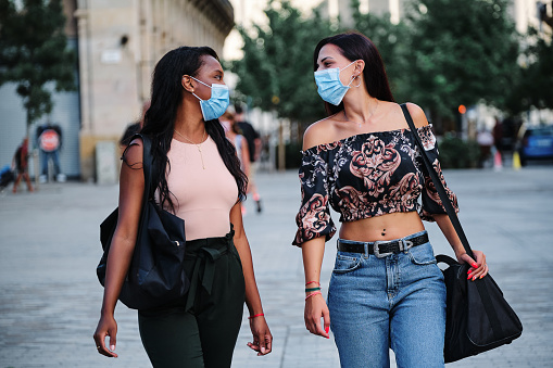 Two multiethnic female friends with protective facial mask walking in the street