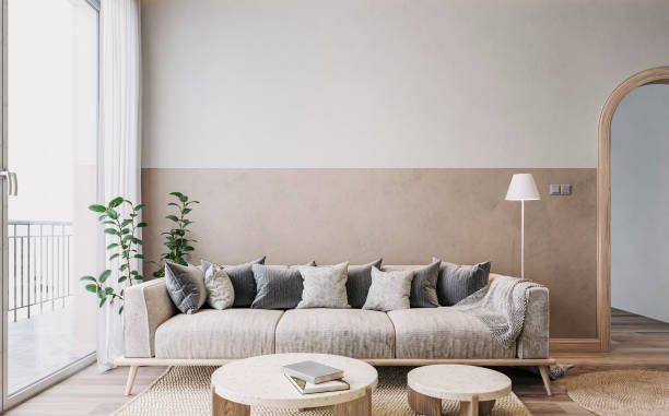 istock Empty nostalgic retro living room with beige sofa, colored cushions, marble coffee tables, and decoration in front of a beige and white colored wall 1459013604