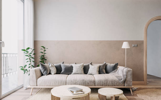 Empty nostalgic retro living room with beige sofa, colored cushions, marble coffee tables, and decoration in front of a beige and white colored wall stock photo