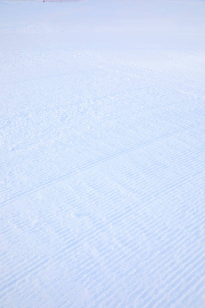 Close-up straight line rows of freshly prepared groomed ski slope piste with bright shining sun and clear blue sky background. Snowcapped mountain downhill landscape at europe winter skiing resort