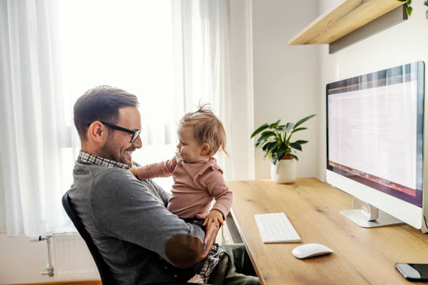 A casual businessman sits at home office with his daughter and playing with her on a break. stock photo
