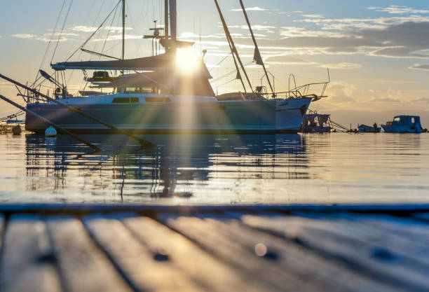 die strahlen der untergehenden sonne hinter dem schiff auf dem pier - sailboat sunset nautical vessel sun stock-fotos und bilder