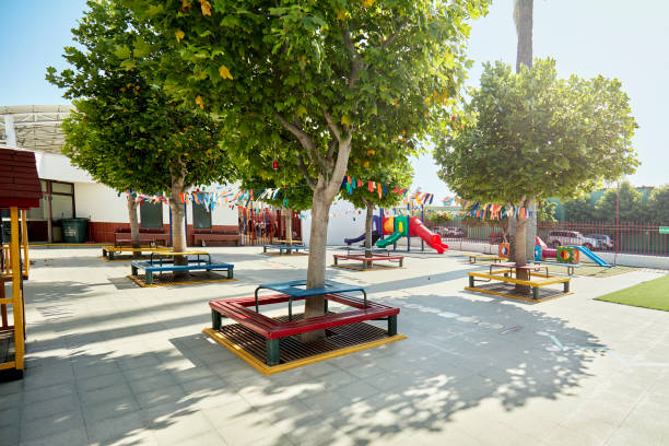 Leafy springtime trees surrounded by multicolored benches and bunting with playground equipment in background.