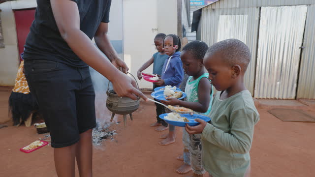 Poverty in Africa. Hungry Black African children holding out plates while a charity organisation distributes food