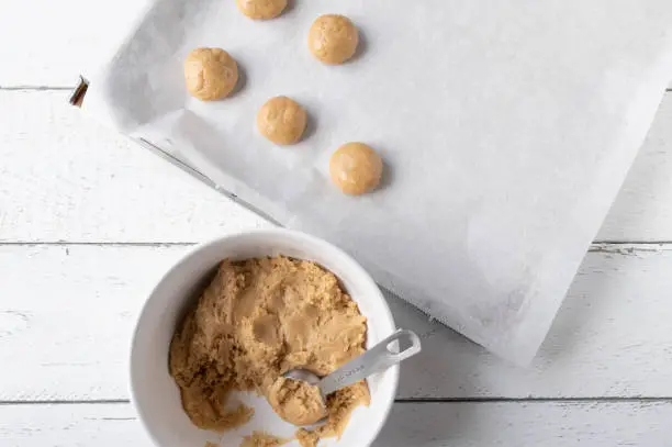 Homemade fresh dough for gingerbread cookies in a bowl with spoon and a baking sheet for baking the christmas cookies. Flat lay on white background with space for text.