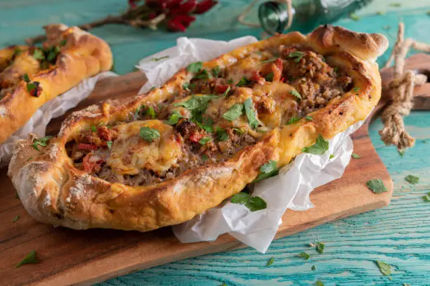 Delicious homemade turkish pide or flatbread with ground beef, tomatoes, bell peppers, garlic, onions and parsley. Topped with melted cheese. Served on wooden, colorful background. closeup and front view