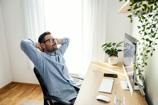 A remote worker is leaning back in chair and relaxing after hard work.