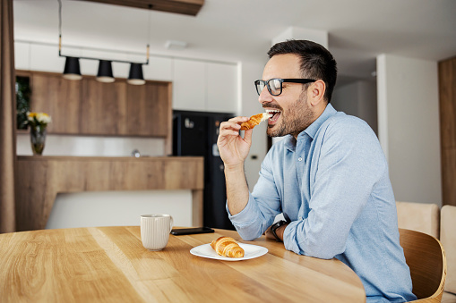 A man eating croissant for breakfast at home.