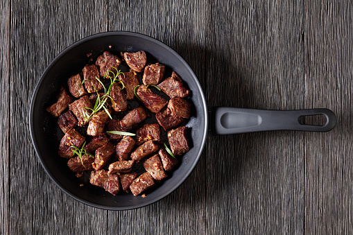seared juicy new york strip steak bites with butter, rosemary and garlic on skillet on dark wood table, horizontal view from above, flat lay, close-up