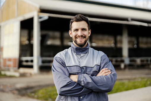 A smiling farmer proudly stands in front of the barn outside and smiles at the camera. Modern farming and livestock.
