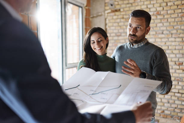 istock Happy couple talking about housing project with their agent at construction site. 1459017703