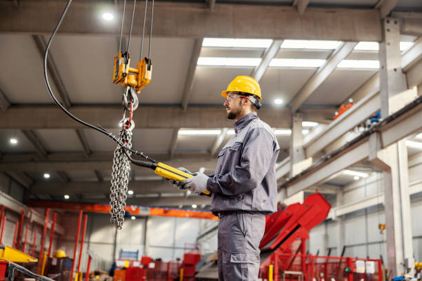 A heavy industry worker relocates chains on hook and commands while standing in a metalwork factory. stock photo