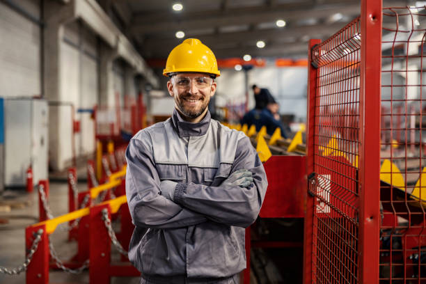 A heavy industry worker stands in a facility with arms crossed and smiling at the camera. Proud metallurgy and heavy industry worker stands in a factory with arms crossed and smiles at the camera. manufacturing occupation stock pictures, royalty-free photos & images