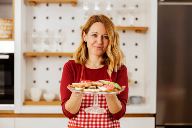 portrait of a happy woman holding plate with christmas cookies and smiling at the camera. - pastry bakery biscuit cookie imagens e fotografias de stock