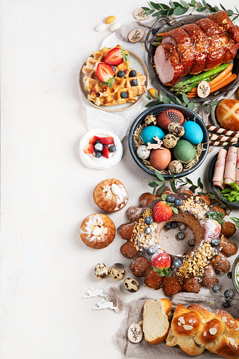 Traditional Easter dinner or  brunch with ham, colored eggs, hot cross buns, cake and vegetables. Easter meal dishes with holday decorations. Top view, copy space