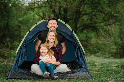 Happy family holidays in a tent with a child in nature. Mother, father and child enjoying a camping holiday in countryside. oncept of summer vacation and travel, trip. Campsite.