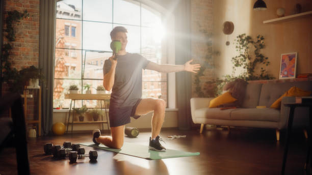 istock Strong Athletic Fit Young Man Standing on One Knee and Lifting a Heavy Kettlebell, Doing Core Strengthening Exercises During Morning Workout at Home in Bright Apartment. Health and Fitness. 1459025773