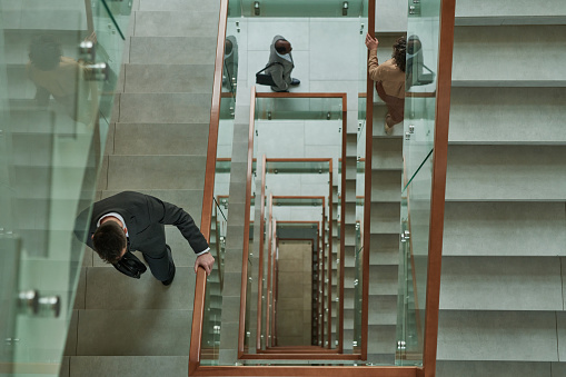 Above shot of three business people in formalwear walking upstairs and between staircases inside modern building while going to work