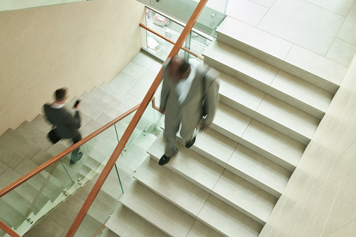 Blurred motion of two multicultural male employees in formalwear walking downstairs along staircase while leaving office center after work