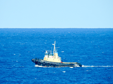A tugboat off Bondi Beach heads north towards Sydney Harbour on a windy and sunny afternoon of 24 January 2023.  The heat of the exhaust coming out of the funnel is visible. This image was taken from the cliffs on the southern end of the beach.