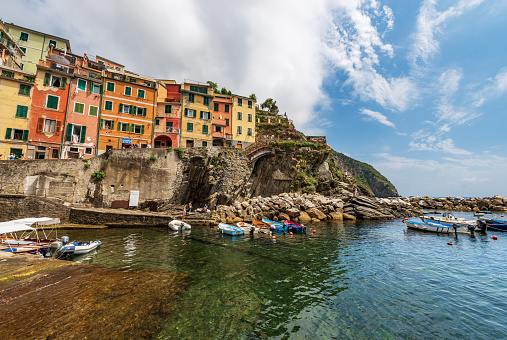 Riomaggiore, Liguria, Italy - July 8th, 2021: The famous Riomaggiore village, view from the small port, Cinque Terre National Park in Liguria, La Spezia, Italy, Europe. UNESCO world heritage site. A group of tourists visits the ancient village on a sunny summer day.