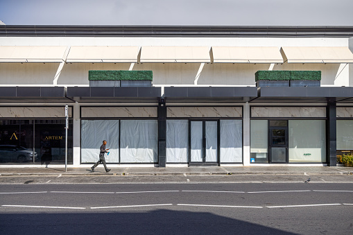 Cape Town, South Africa - December 9th 2022: Pedestrian walking in front of a closed shop with blinded windows