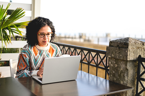 mid adult woman typing on computer outdoors.