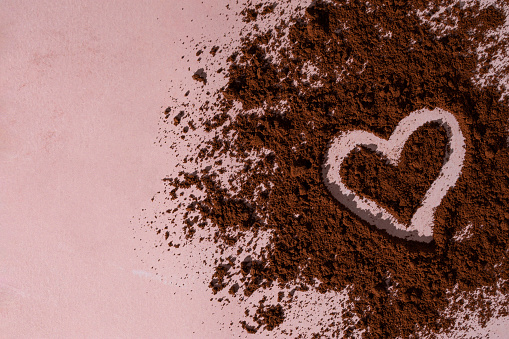 Heart made from ground coffee on a romantic pink background. Creative coffee love concept.