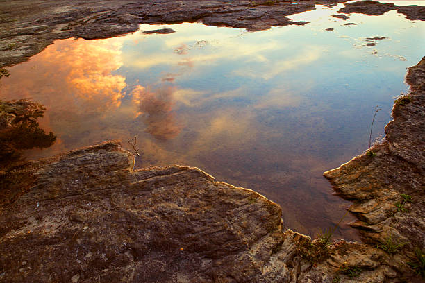 Lonely stone in the river. Reflection of the sky in water, free space for text.