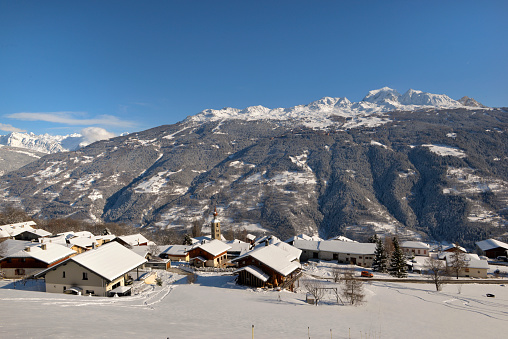 alpine village with snowy roofs in tarentaise valley view on snowcapped mountains under blue sky
