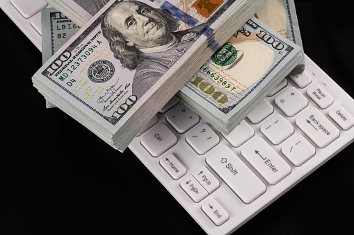 Packs of American dollars lie on a white computer keyboard on a black background