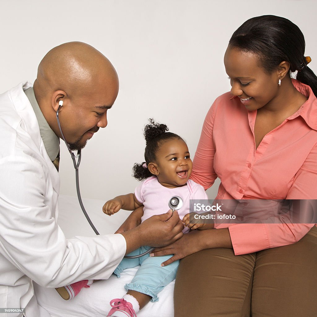 Mother holding baby for pediatrician to examine. African-American male doctor examining baby girl with mother watching. African Ethnicity Stock Photo