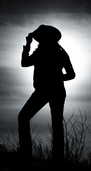 A silhouette of a cowgirl tipping her hat to the setting sun.