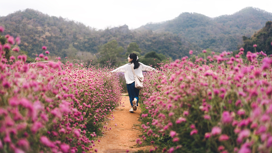 Outdoor travel in nature concept. Top of mountain rear view young adult asian woman running in flower blossom park field mood on spring or summer. Banner size background.