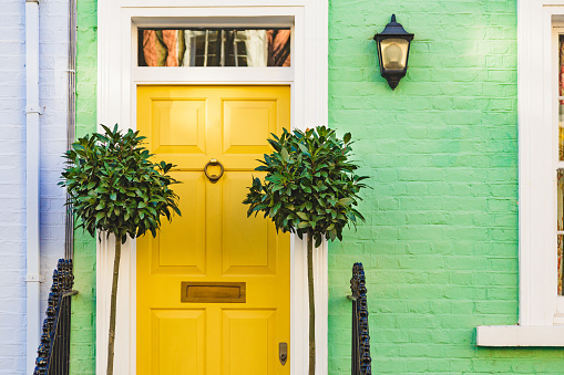 The colorful green pastel facade of a traditional London mews house with a vibrant yellow front door.