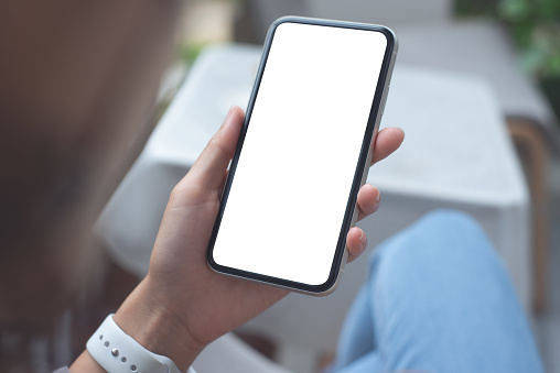 Cell phone mockup image blank white screen. Woman hand holding texting using mobile phone at coffee shop. Background and copy space for advertisement. Person connecting the internet at cafe