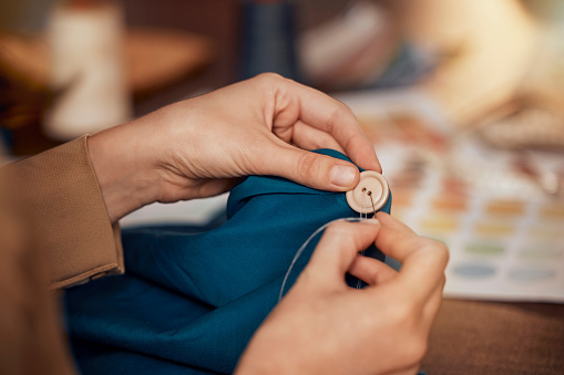 Womab, hands and sewing clothes button in studio for designer wear, fashion garment and creative fabric design. Tailor, boutique startup and fashion designer hand or seamstress working on clothing