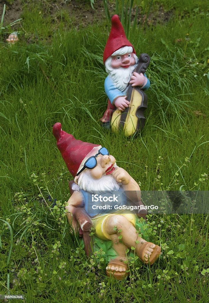 Lounging garden gnome statues in the grass A garden gnome is taking a sunbath while listening to the musician. The third one is hiding! Garden Gnome Stock Photo
