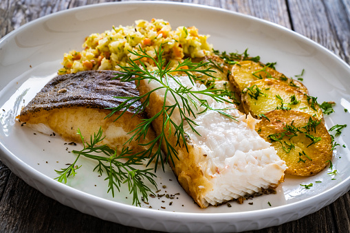 Fried halibut and potatoes with cabbage salad on wooden table
