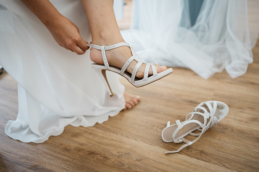 bride sits on chair and puts on her wedding shoes