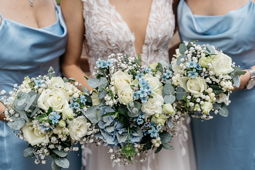 bride with two maids of honor in blue dresses holding their flower bouquets