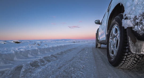 ruota panoramica di un'auto 4x4 ghiacciata su una strada totalmente innevata con tracce di pneumatici che arriva fino all'orizzonte con un'alba islandese viola e magica. la luce dell'alba si riflette nell'auto. - off road vehicle 4x4 snow driving foto e immagini stock