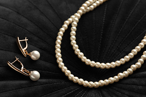 Elegant necklace and golden earrings with pearls on black fabric, closeup