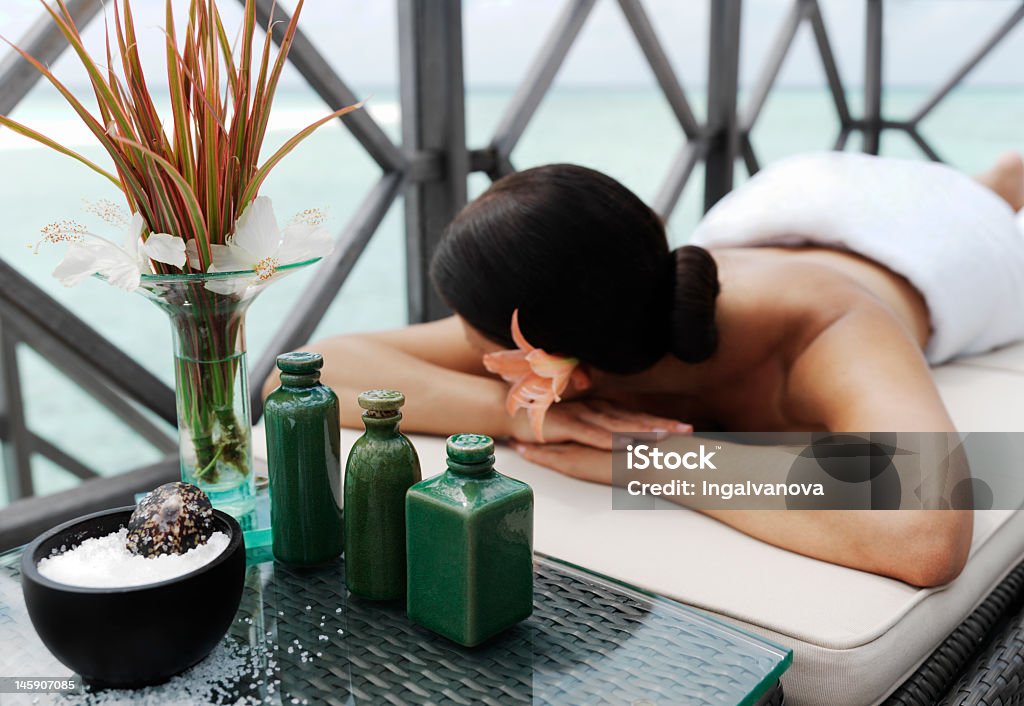 Unidentifiable woman lying face down on spa treatment bed  beautiful woman getting spa treatment at daylight near the ocean Adult Stock Photo