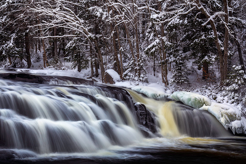A long exposure rendered Buttermilk Falls in Long Lake, New York, as silky smooth on a cloudy winter day. Ice lines the shore and snow covers the trees above the waterfall. Buttermilk Falls is an easily accessible waterfall just minutes from the town of Long Lake, and is beautiful in any season.